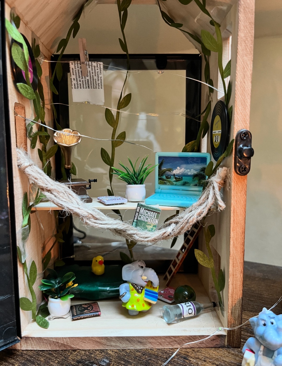 Inside a miniature house: rope hammock, tiny laptop, gramophone, trailing vines